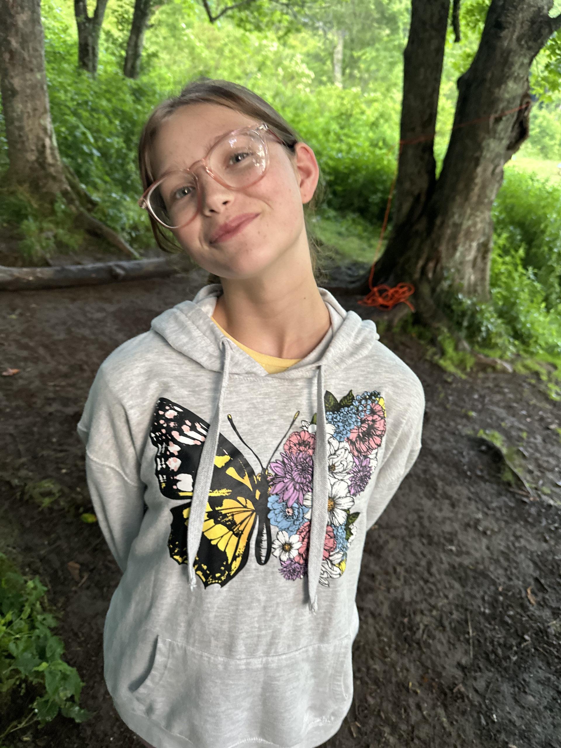 Girl in butterfly shirt smiling while on a hike with Eremos. | Eremos | Multi day Backpacking Experience